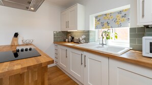 A modern kitchen with white cabinets, a wooden countertop, a built-in microwave, and a window with floral curtains.