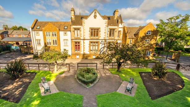 A traditional building with a symmetrical facade, a central entrance, and a well-maintained garden with benches.