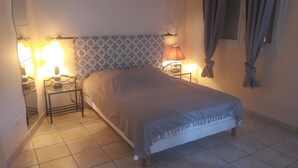 Ein Schlafzimmer mit einem Bett, zwei Nachttischen, einem Fenster mit Vorhängen und einem gemusterten Kopfteil.