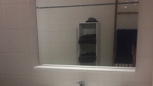 Ein Badezimmer mit einem weißen Waschbecken, einem Spiegel darüber und einem Handtuchhalter zur Rechten.