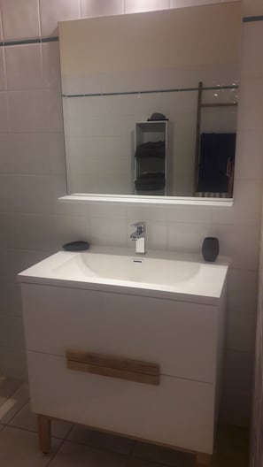 Un baño con un lavamanos blanco, un espejo encima y un perchero a la derecha.
