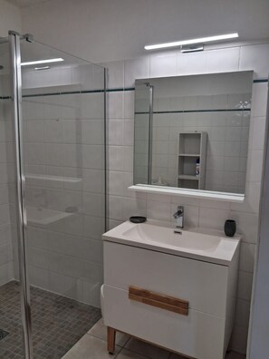 A modern bathroom with a glass shower enclosure, a white vanity with a mirror, and a tiled floor.