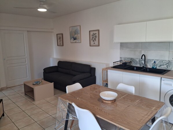 A compact living space with a sofa, a dining table with chairs, a kitchen area with a sink and cabinets, and a door. - T2 Anse à l'Ane, a 5-minute walk from the beach (Les Trois-Îlets)