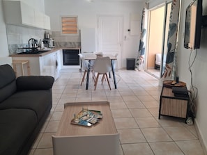 Ein modernes Wohnzimmer mit einer Couch, einem Couchtisch mit Zeitschriften, einer Küche mit Mikrowelle und einem Essbereich mit Stühlen.