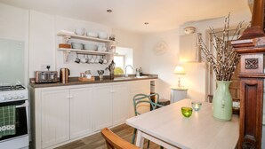 Une cuisine avec des meubles blancs, un fourneau et un coin repas comprenant une table et des chaises.