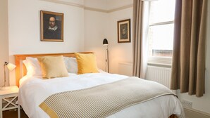 Un lit bien fait, avec une literie blanche et moutarde, une lampe de chevet et deux tableaux encadrés accrochés au mur.
