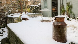 Un espace extérieur rustique agrémenté d’un mur de pierres, d’un conteneur en métal et d’une petite table recouverte de neige.