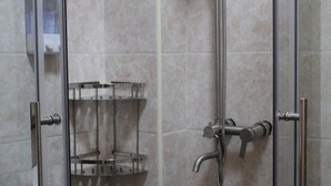 Un espace douche doté d’une porte en verre, d’un pommeau de douche en métal et d’une étagère.