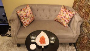 Un salon avec un canapé, deux coussins à motifs, une table basse ronde ornée d’une feuille décorative, deux verres et un petit objet blanc.