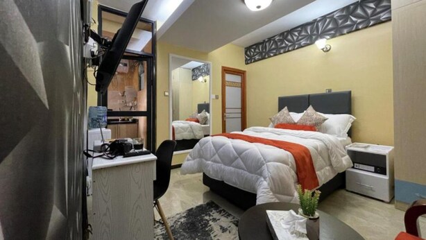 Une chambre d’hôtel comprenant un lit, des tables de chevet, un bureau avec une chaise, un miroir et un panneau décoratif mural.
