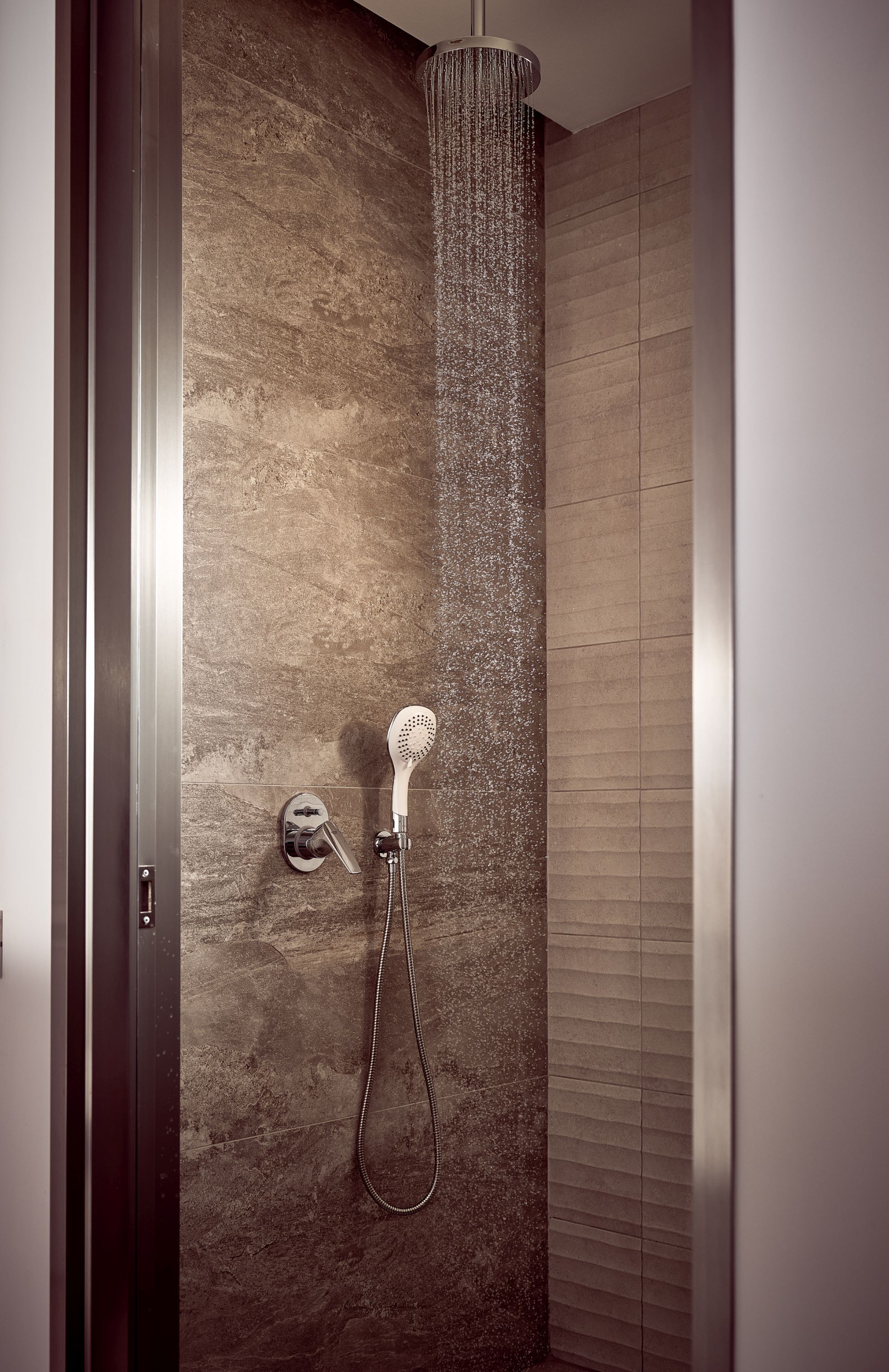A shower with a handheld showerhead and a wall-mounted control.