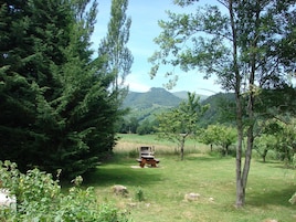 A picnic table in a grassy area with trees and mountains in the background.