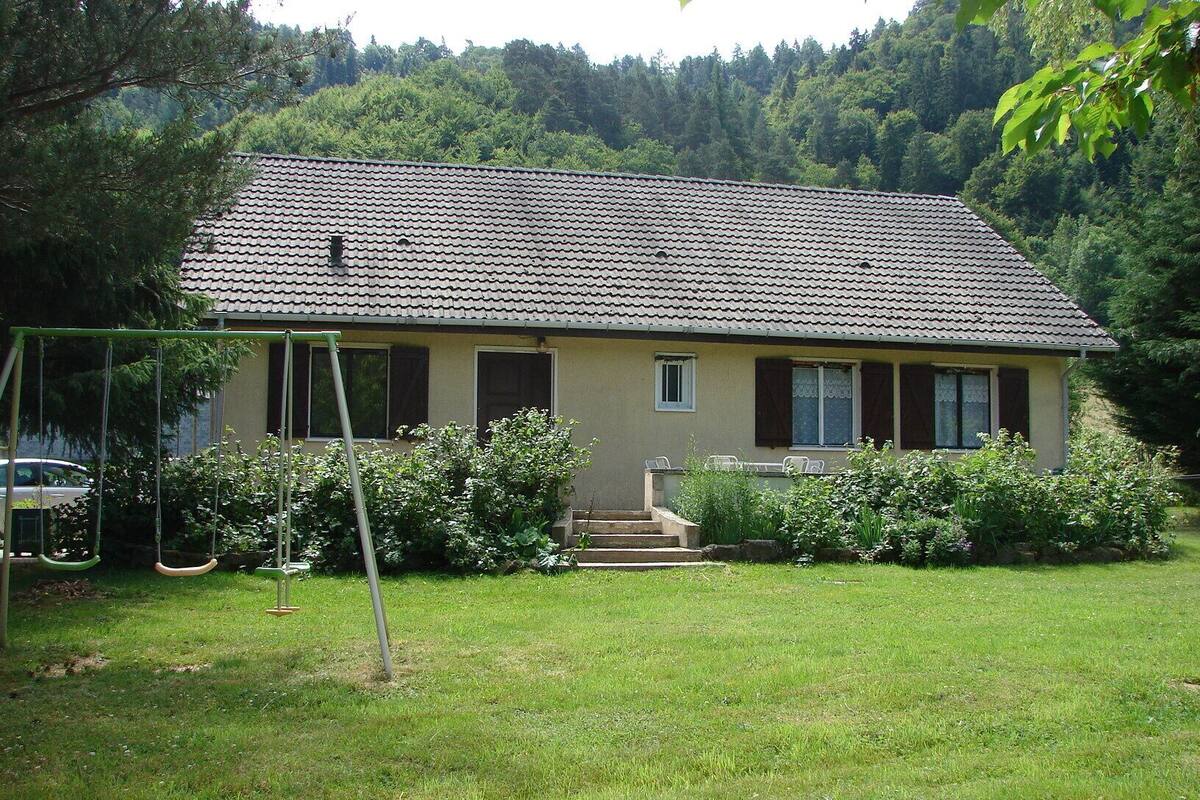 A single-story house with a tiled roof, a front porch, and a swing set in the yard.