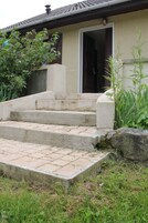 A house with a concrete staircase leading to a door, surrounded by grass and plants.