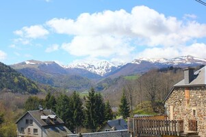 A stone building with a balcony, surrounded by a mountainous landscape with snow-capped peaks.