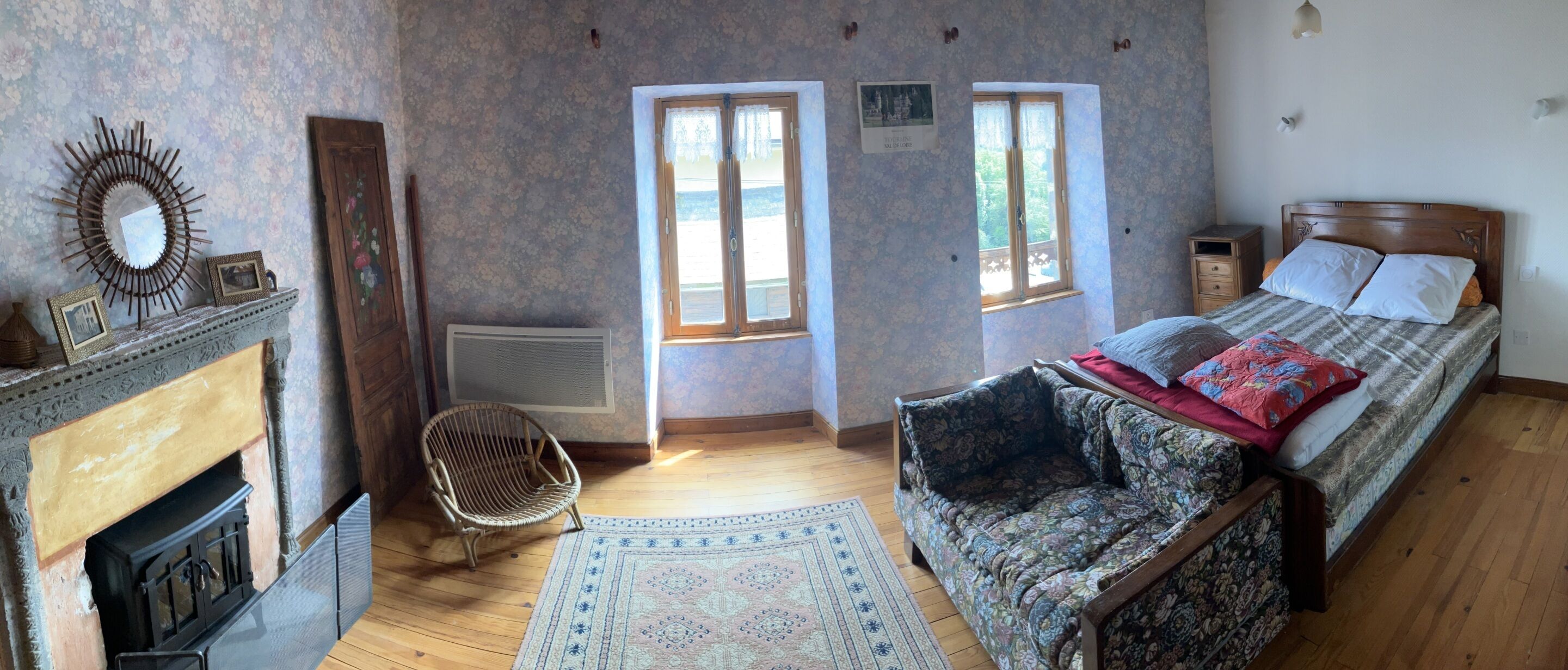 A bedroom with a bed, a chair, a fireplace, and two windows.