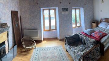 A bedroom with a bed, a chair, a fireplace, and two windows.