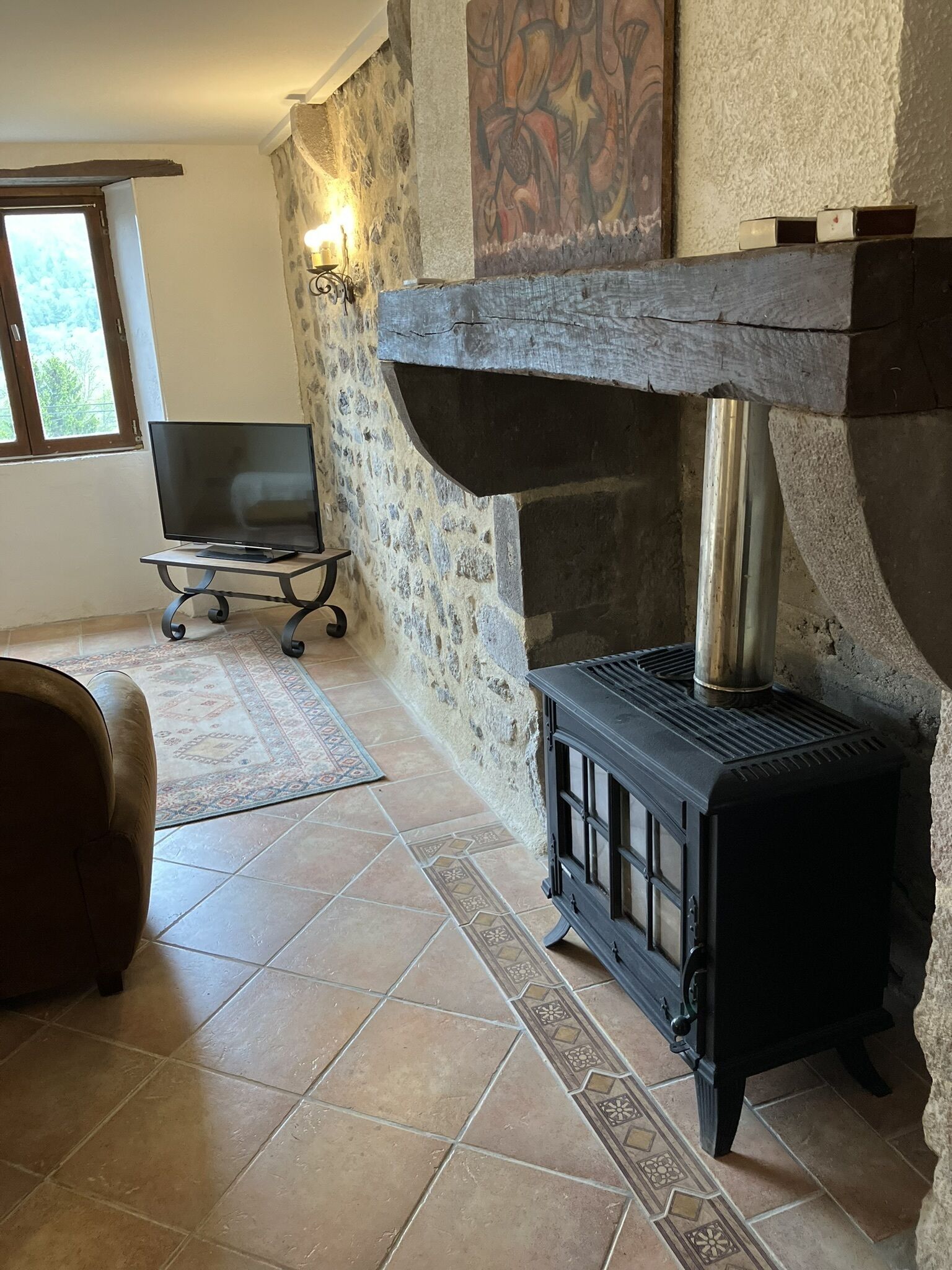 A cozy room with a stone fireplace, a flat-screen TV on a stand, and a patterned rug on the tiled floor.