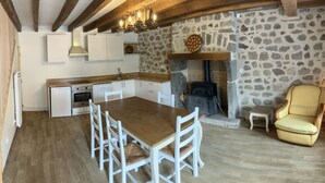 Una cocina con pared de piedra, escalera de madera y zona de comedor con sillas blancas.