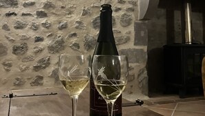 Una botella de vino y dos copas sobre una mesa de madera en una habitación con pared de piedra y chimenea.