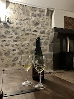 Una botella de vino y dos copas sobre una mesa de madera en una habitación con pared de piedra y chimenea.