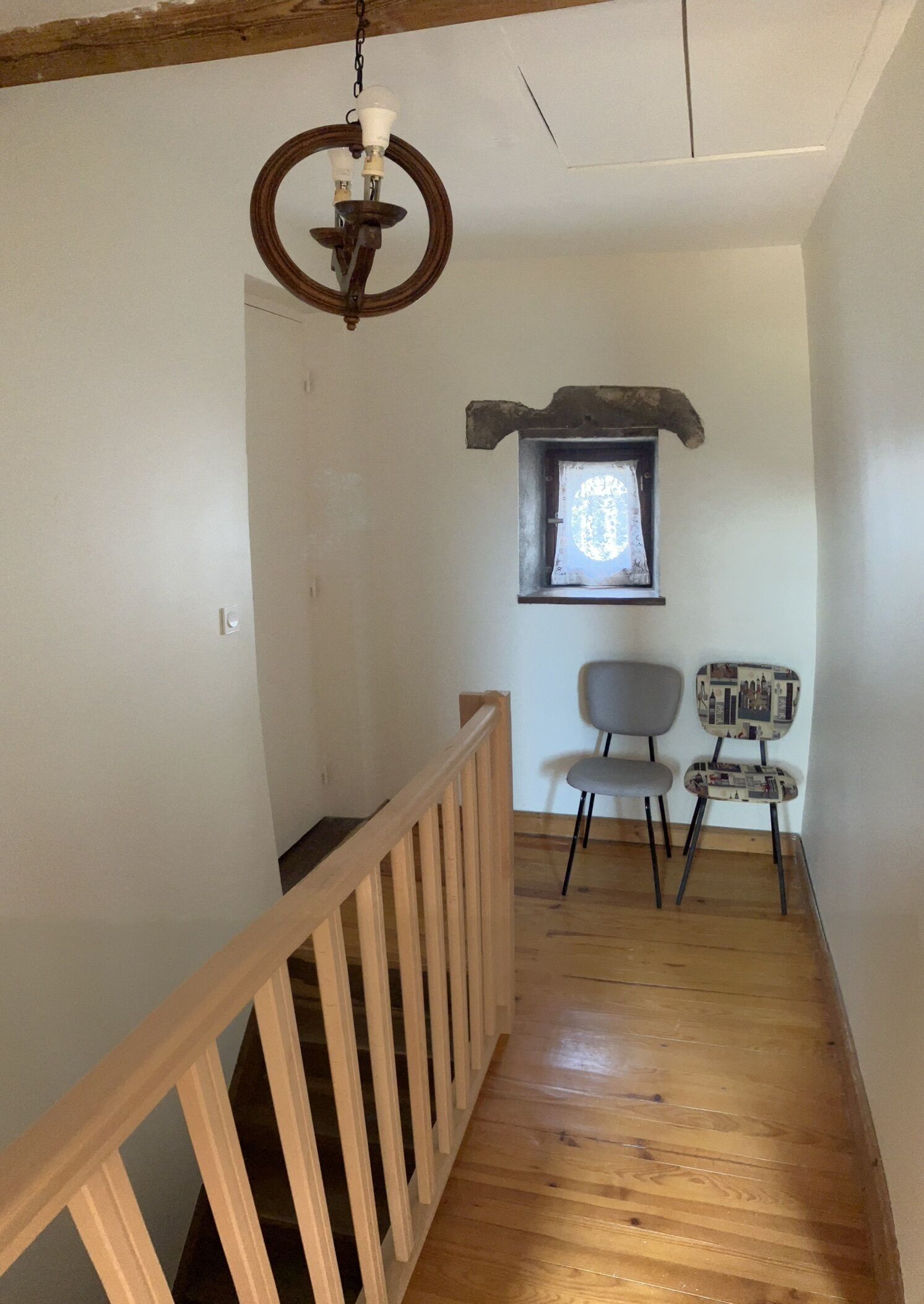 A wooden staircase with a railing, a small window with a decorative frame, and a chair with a patterned backrest.