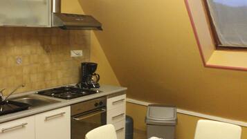 A kitchen with a stove, oven, and sink, a dining table with a floral tablecloth, and a window with a pink frame.