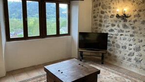 Una habitación con un ventanal grande, un televisor de pantalla plana, un cofre de madera y una alfombra estampada.