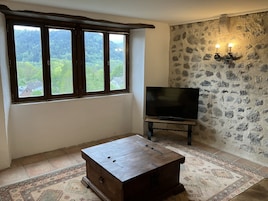 Una habitación con un ventanal grande, un televisor de pantalla plana, un cofre de madera y una alfombra estampada.