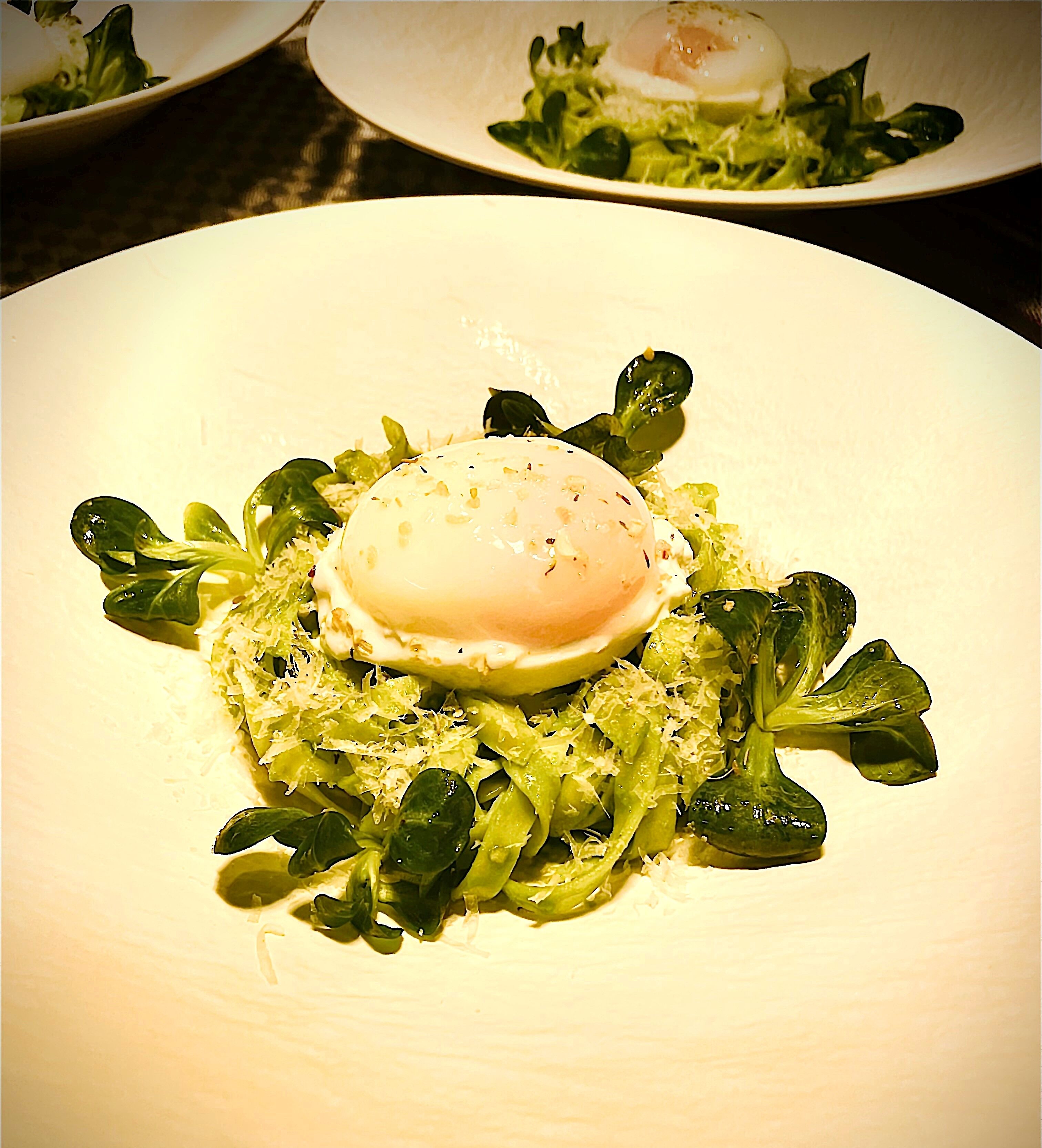 A plate of food with a poached egg, greens, and a creamy sauce.