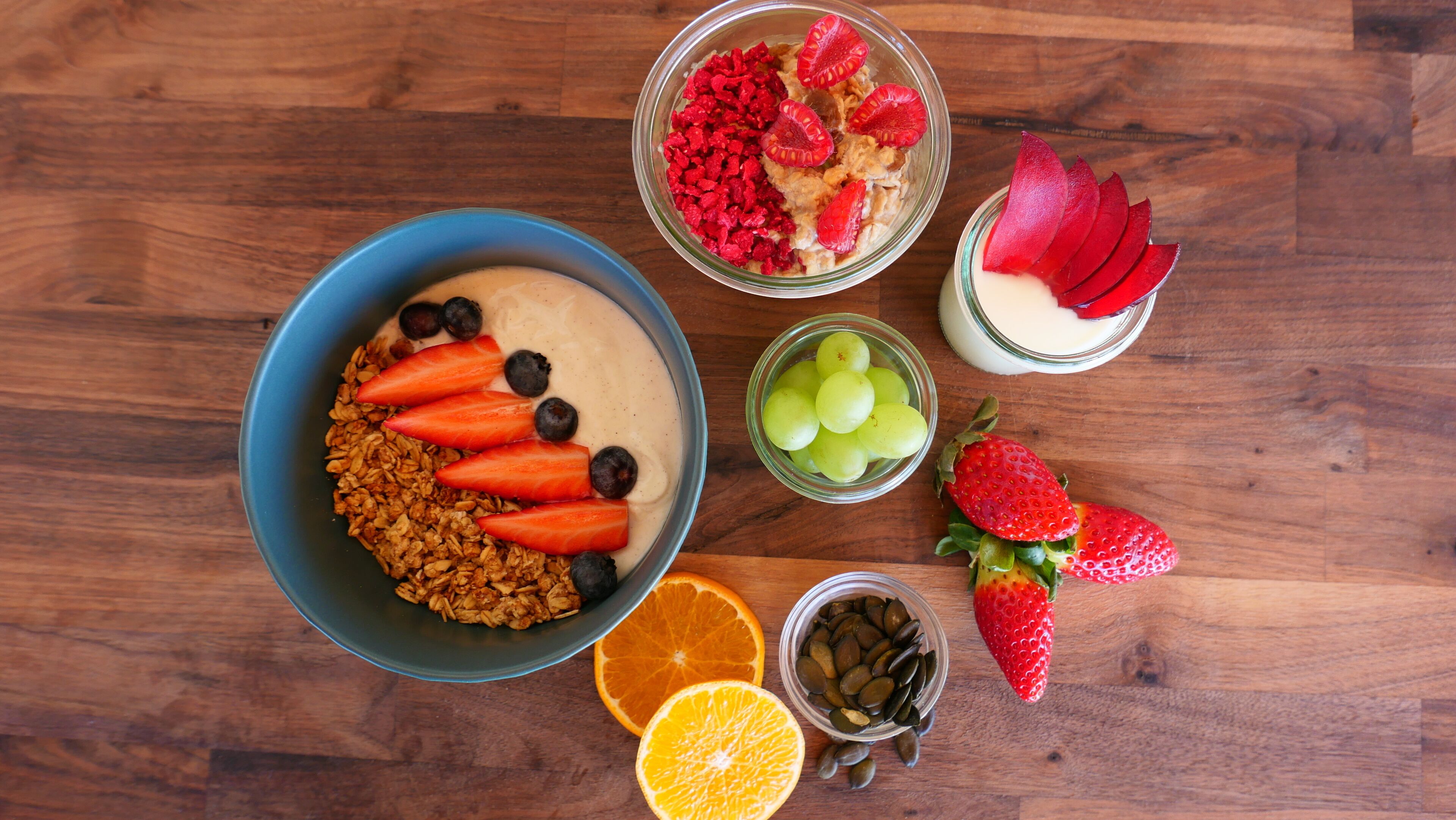 A breakfast spread with various fruits, granola, and yogurt on a wooden table.