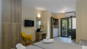 Ein Hotelzimmer mit zwei Betten, einem Schreibtisch mit Computer, einem gelben Stuhl, einem Fernseher und Blick auf die Küche und den Balkon.