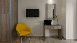 Ein modernes Zimmer mit einem Holzschrank, einem gelben Sessel, einem Flachbildfernseher, einem Schreibtisch mit einem Laptop und einem Spiegel.