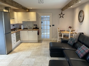 A compact kitchen with modern appliances, a dining area with a wooden table and chairs, and a black leather sofa with a plaid pillow.