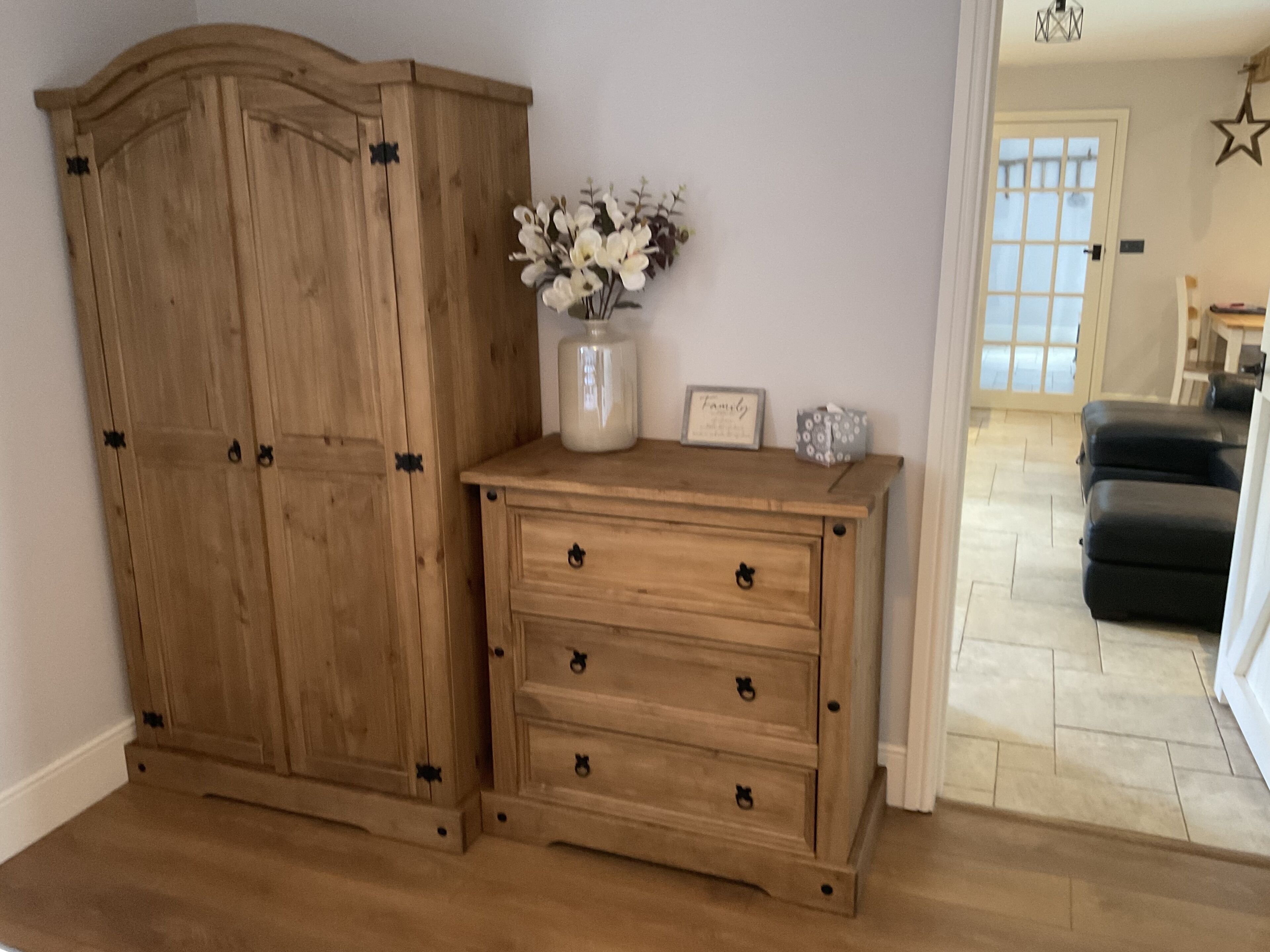 A wooden wardrobe with a vase of flowers and a framed picture on top.