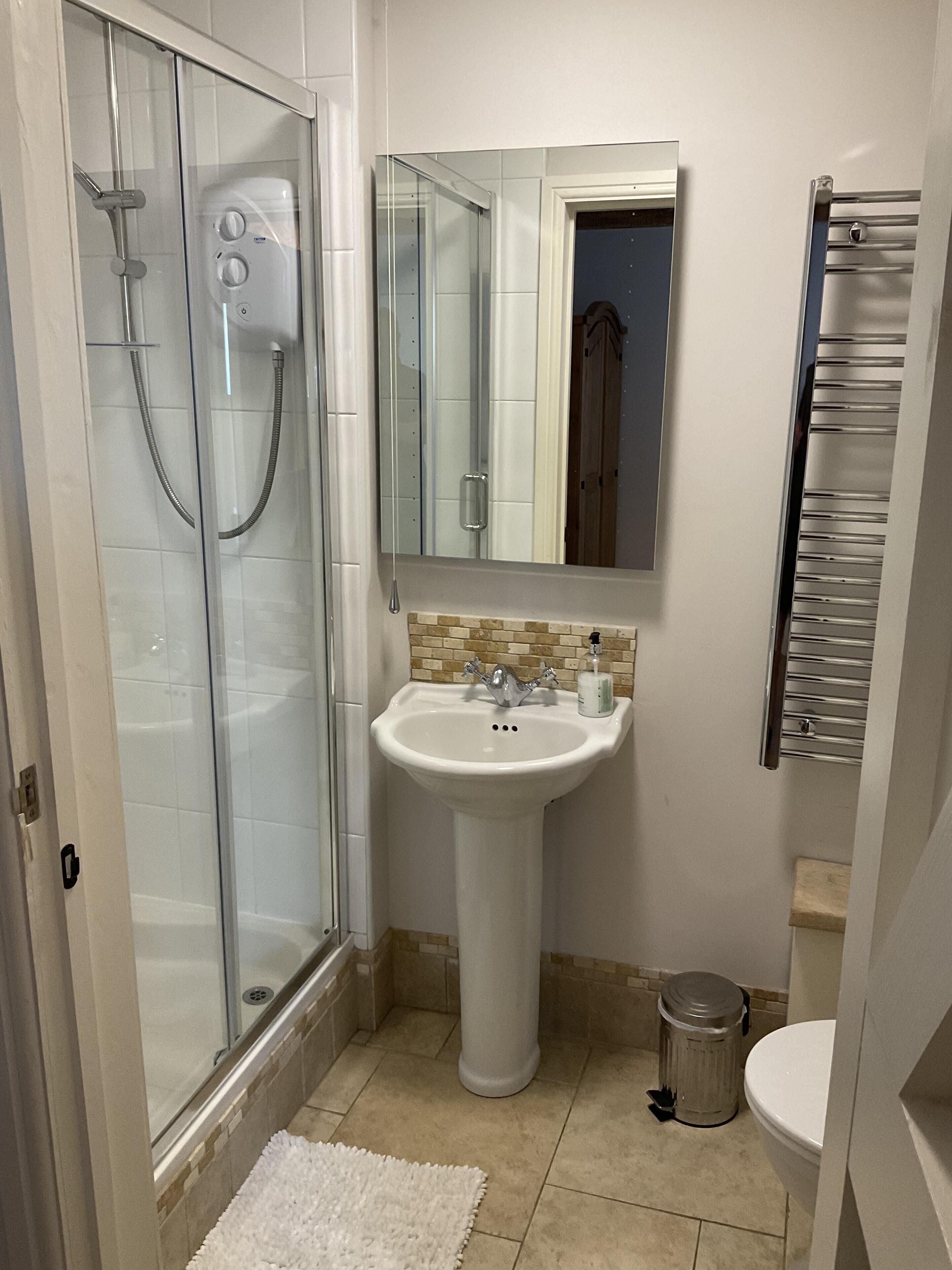 Een badkamer met een douche met glazen wanden, een wastafel op een voetstuk, een spiegel en een toilet.