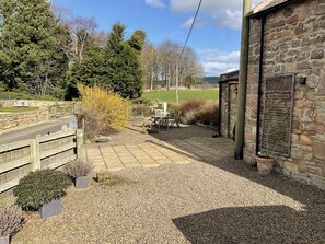 Un edificio de piedra con un patio de grava, mobiliario exterior y vistas a un campo verde.