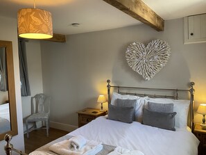 A neatly arranged bedroom with a bed, bedside lamps, a chair, and a decorative heart-shaped wall piece.
