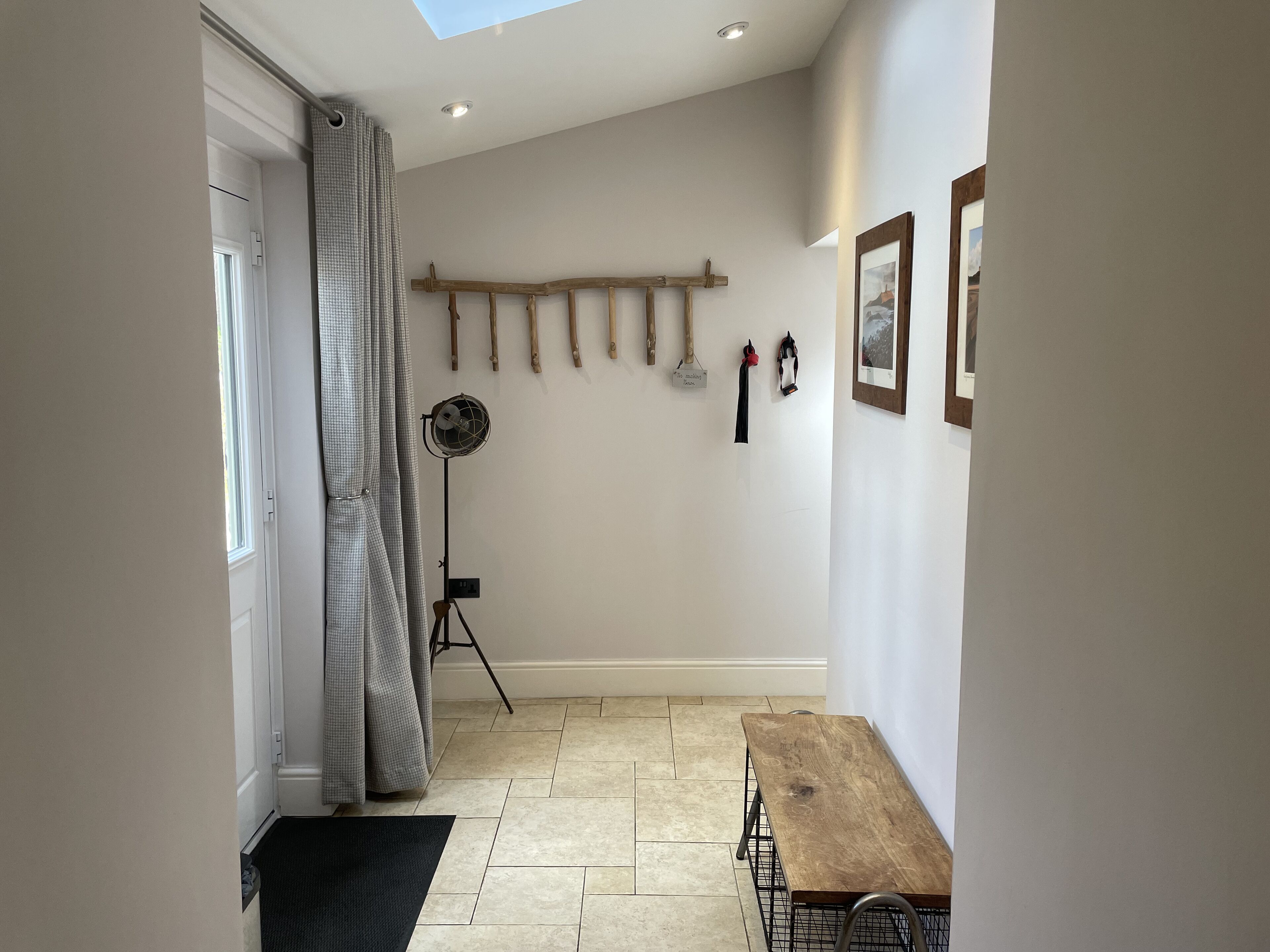 Un couloir étroit avec un banc en bois, un ventilateur sur pied et une porte avec un rideau.