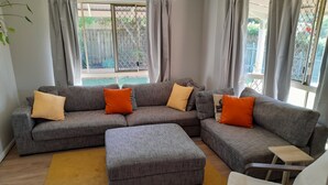 A living room with a grey sectional sofa, a yellow rug, and a white armchair. - Spacious Family house in great location. (Tanah Merah)
