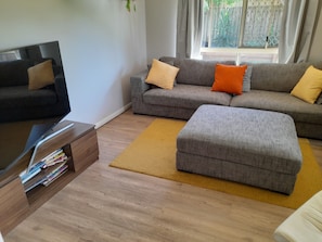 Un soggiorno moderno con un divano grigio, un poggiapiedi abbinato, un tavolino da caffè in legno e una TV su un mobile.