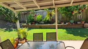 A covered patio with a glass-top table and chairs, surrounded by potted plants and a wooden fence. - Spacious Family house in great location. (Tanah Merah)