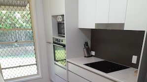 A modern kitchen with white cabinetry, a black stovetop, and a wooden floor. - Spacious Family house in great location. (Tanah Merah)