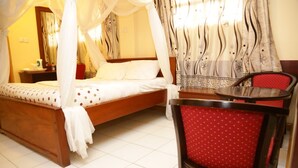 A bedroom with a wooden bed, a red chair, a small table, and a canopy bed. - Roza Guests House (Naivasha)