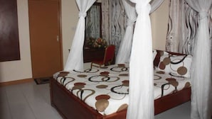 A bedroom with a four-poster bed, a wooden door, and a chair. - Roza Guests House (Naivasha)