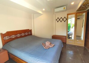 A neatly made bed with a patterned bedspread, a wooden headboard with a geometric design, a small bedside table, and a mirror cabinet with a door.