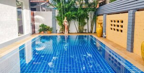 A swimming pool with blue tiles, surrounded by a white wall and a yellow fence with a decorative vase.