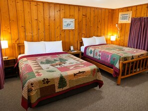 A room with two wooden beds, a nightstand, a lamp, a framed picture on the wall, and a window with curtains.