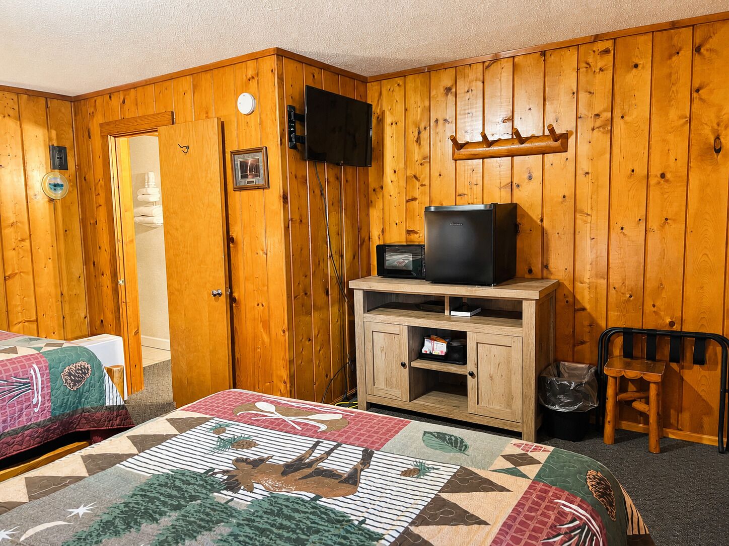 A wooden room with a bed, a TV on a wooden stand, a microwave, and a small cabinet.