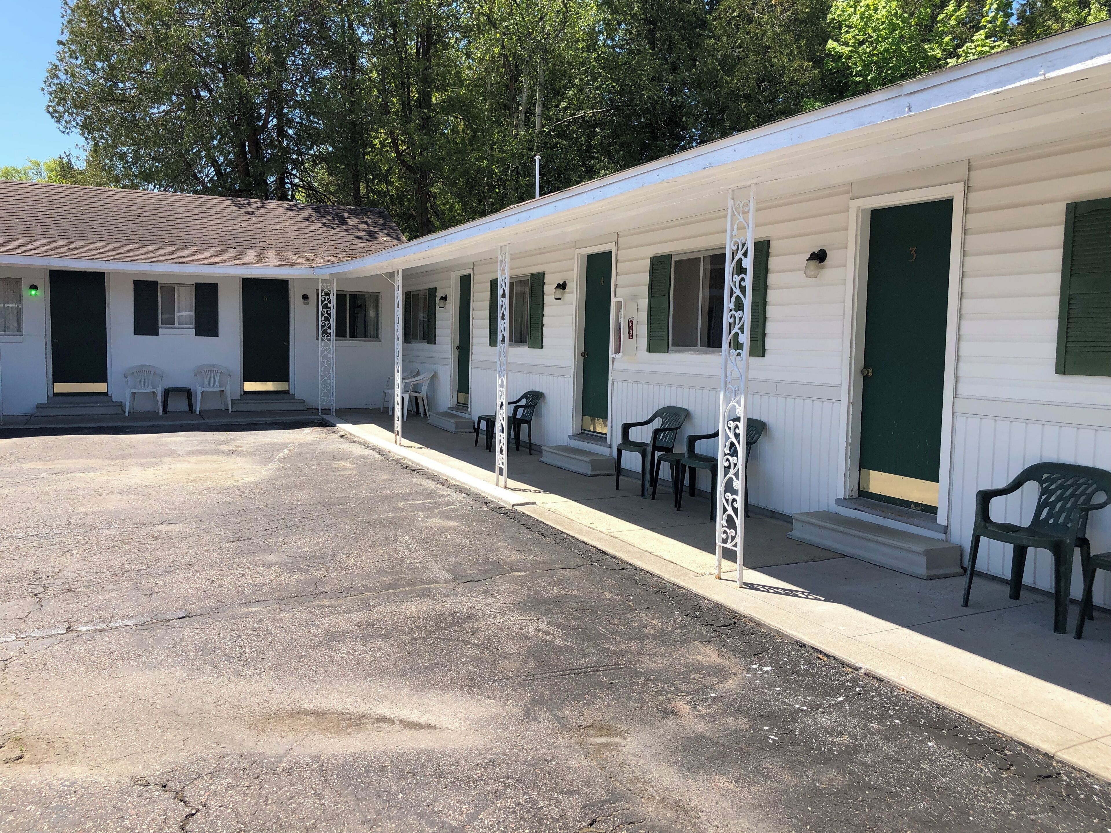A row of motel rooms with green doors and white walls, each with a small porch and a single chair.